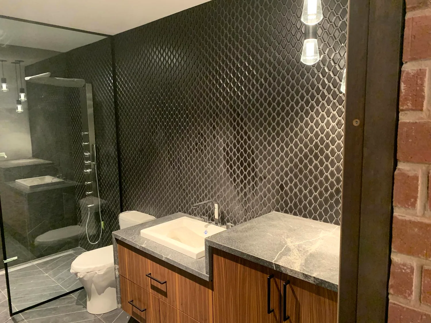 Dark fishscale wall against the original brick, walnut vanity