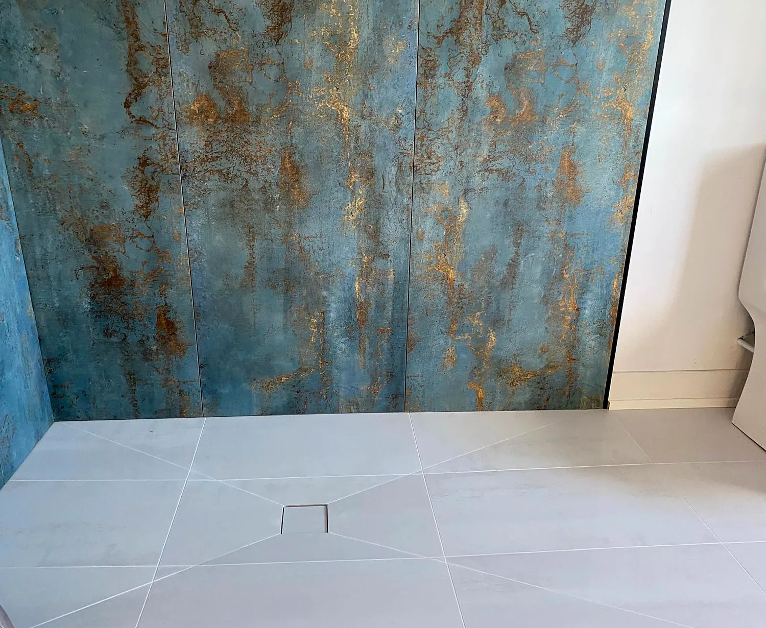 Oxidised blue-green slab wall over a pale large-format floor